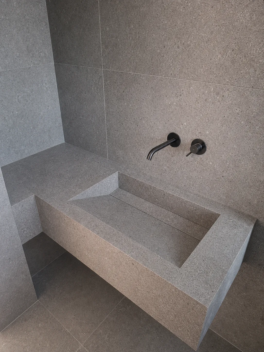 Grey large-format porcelain wet room wall with precise cuts around wall-mounted brassware